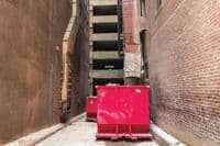 red dumpster in alley between two brick buildings